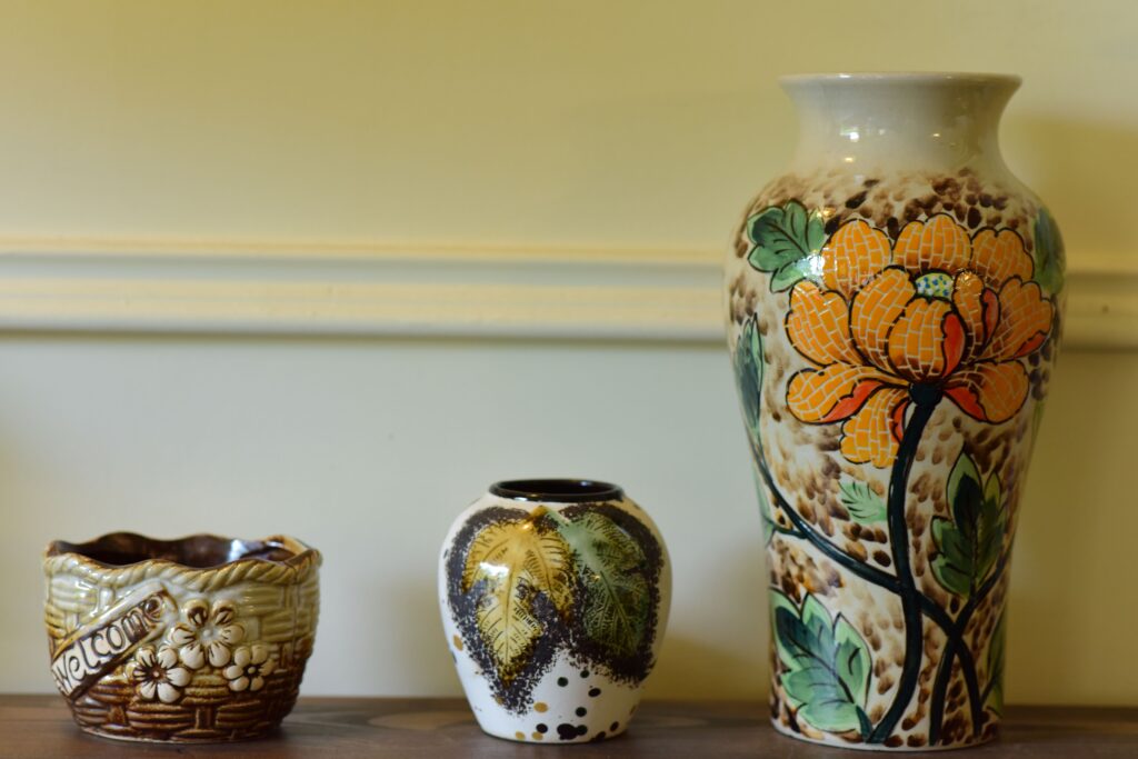 Three decorative ceramic vases with floral designs on a wooden shelf against a neutral background.