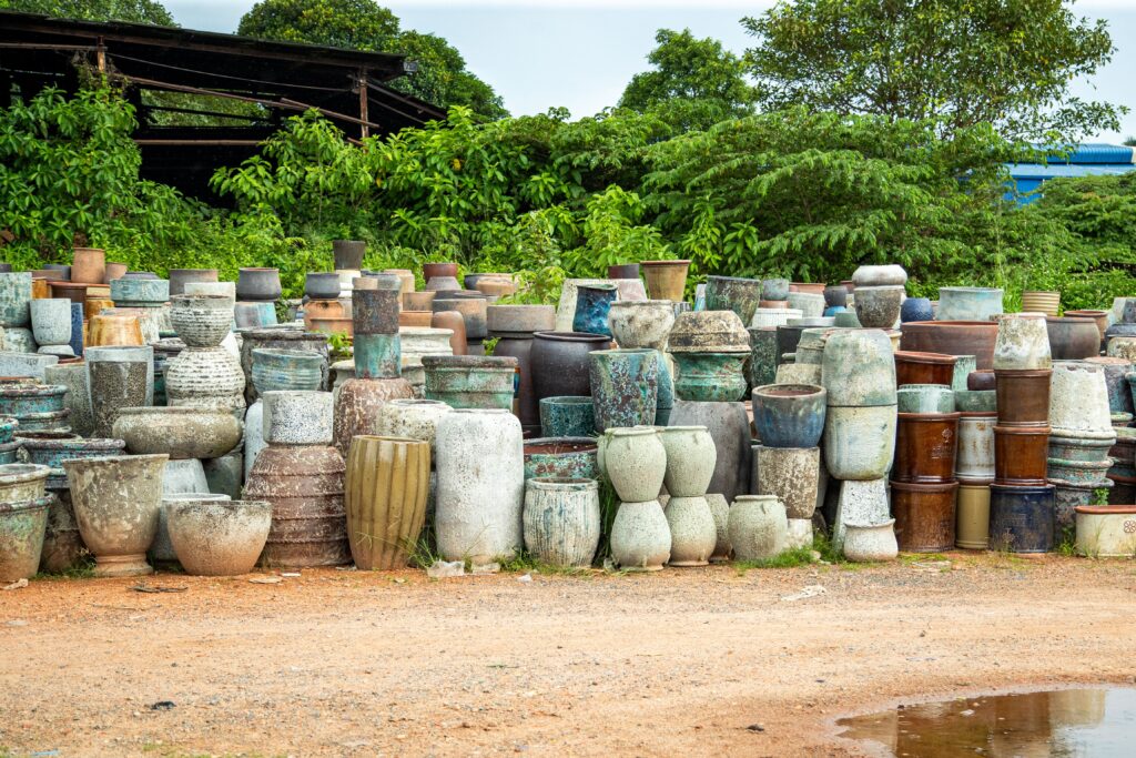 Colorful ceramic pots displayed outdoors with lush green backdrop and rustic setting.